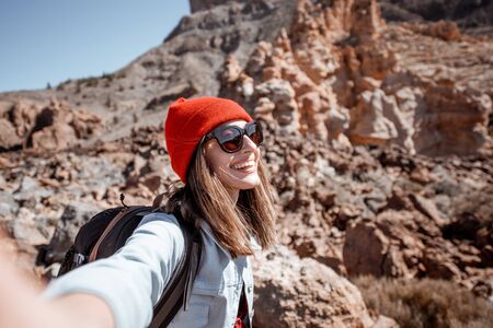 Self portrait of a stylish carefree woman dressed casually in jeans and red hat enjoying travel on the rocky terrain on a sunny dayの写真素材