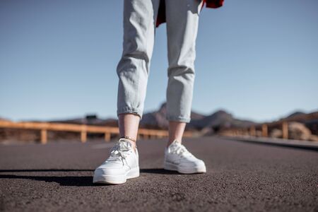 Woman on the desert road, close-up view on the women's legs in white sneakersの写真素材