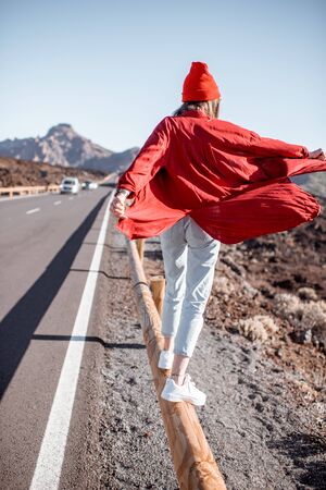 Lifestyle portrait of a young woman stylishly dressed in red walking on the road fence in the midst of volcanic valley on a sunny day. Carefree lifestyle and travel conceptの写真素材