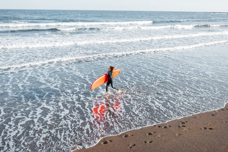 Beautiful sunset view on the ocean beach and surfer walking with red surfboard on a sunset