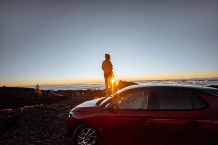 Young woman rocky landscapes above the clouds, standing on the car highly in the mountains. Carefree lifestyle and travel conceptの写真素材