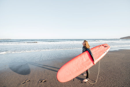 Surfer enjoying beautiful seascape, standing with surfboard on the ocean beach during a sunset, view...