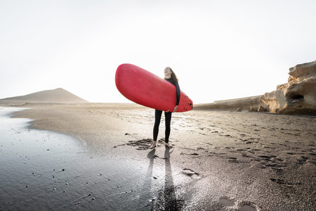 Young surfer in wetsuit running with surfboard to the sea. Summer activities and active lifestyle...