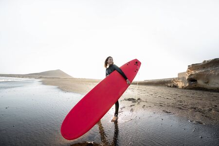 Young surfer in wetsuit running with surfboard to the sea. Summer activities and active lifestyle conceptの写真素材