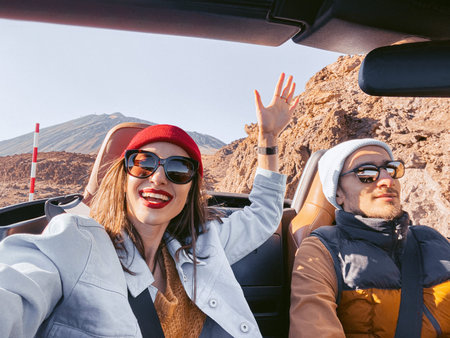 Selfie portrait of a happy couple driving convertible car on the desert road. Carefree lifestyle and...