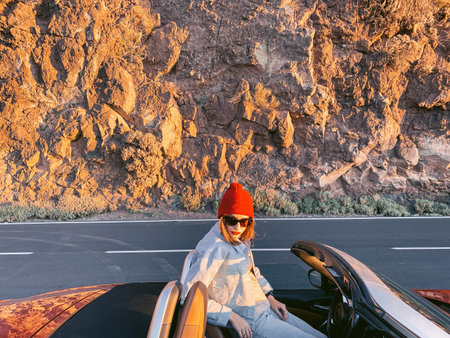 Woman enjoying beautiful sunset while travel mountains by convertible car. Image made on mobile...