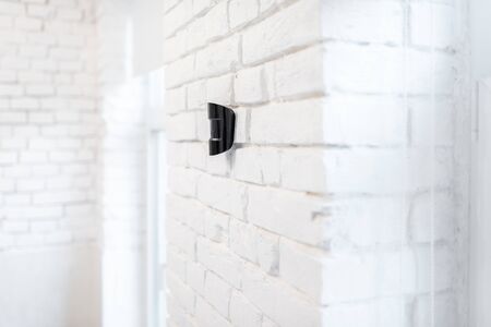 Black wireless motion sensor of alarm system mounted on the white brick wall indoorsの写真素材