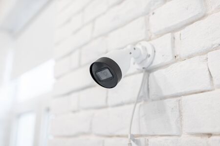Surveillance ip camera mounted on the white brick wall indoors. Home video surveillance conceptの写真素材