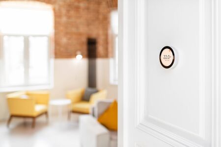Round smart thermostat with touch screen installed on the wall indoors. Smart home heating regulation conceptの写真素材