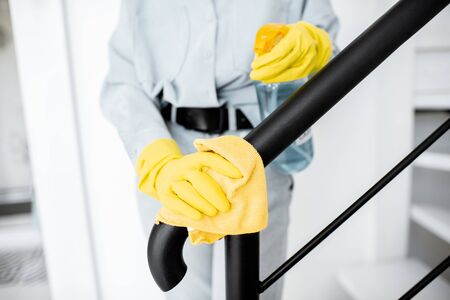 Woman in protective gloves disinfecting stair railings while cleaning at home, close-up view on handsの写真素材