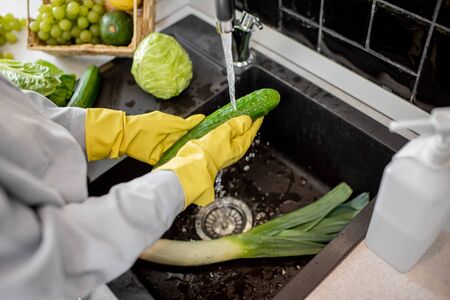 Woman in protective gloves washing fresh vegetables at home on the kitchen, detergent in the foreground. Concept of hygiene during the coronavirus epidemicの写真素材