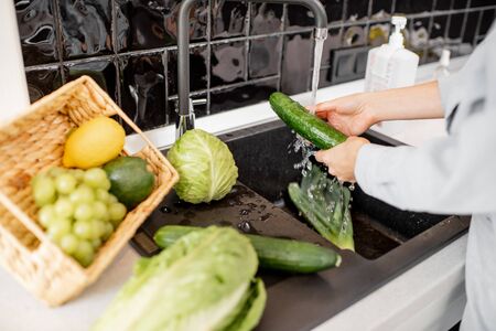 Woman washing fresh vegetables on the kitchen at home, close-up on handsの写真素材