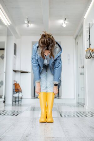 Woman wearing yellow boots and raincoat at the hallway of the apartment. Rainy weather conceptの写真素材