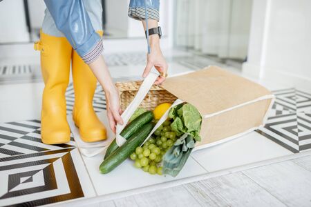 Shopping bag full of fresh vegetables and greens which fell on the floor in the corridor at home, woman in yellow rubber bootsの写真素材
