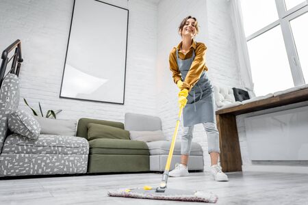 Full length portrait of a young housewife dressed for work in apron, standing with a cleaning mop in the living room of the modern apartmentの写真素材