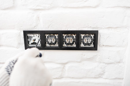Electrician installing sockets and switches on the white brick wall, close-up