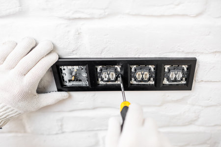 Electrician installing sockets and switches on the white brick wall, close-up