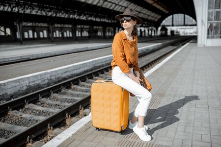 Young female traveler standing with a suitcase at the old train station alone. Travel conceptの写真素材