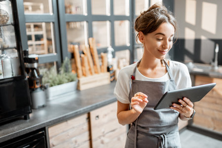 Young saleswoman working with a digital tablet at the counter of cafe or confectionary shop. Concept...