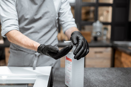 Seller in black gloves disinfecting hands while working in a grocery store or cafe, close-up view....