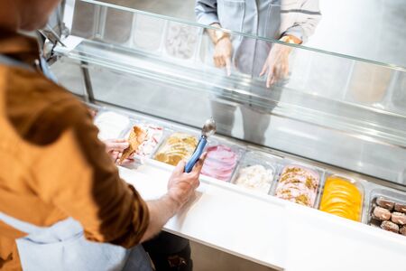 Salesman picking ice cream with a spoon from refrigerator in the store. View from above on a trays full of ice cream with different flavorsの写真素材