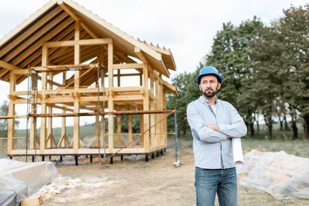 Portrait of an architect or builder with blueprints on the construction site outdoors. The concept of building and designing a wooden frame houseの写真素材