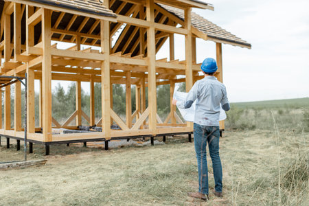 Architect or builder with blueprints on the construction site outdoors. The concept of building and designing a wooden frame houseの写真素材