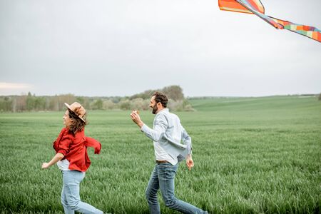 Happy couple having fun together, playing with kite on the greenfield. Happy couple expecting a baby and young family conceptの写真素材