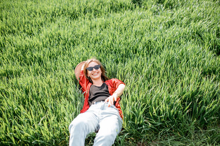 Portrait of a stylish carefree woman lying on the greenfield enjoying nature in springtime, view...