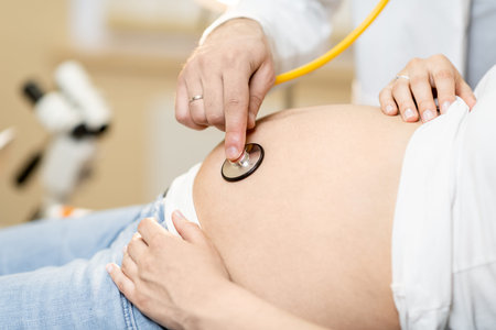 Doctor listening to a pregnant woman's belly with a stethoscope during a medical examination,...