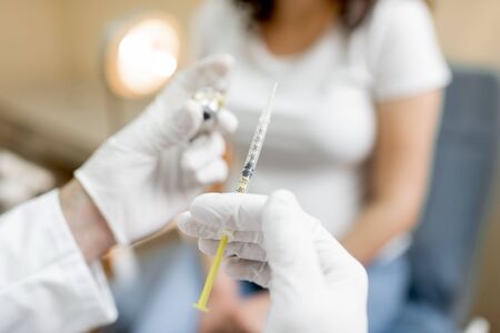 Doctor holding vaccine or some medication in the syringe, preparing for injection for a pregnant woman during a medical procedure in the clinic, close-up viewの写真素材