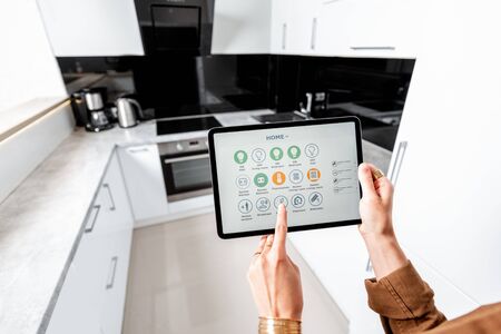 Woman controlling kitchen appliances with a digital tablet, close-up on mobile device with launched smart home application. Smart home conceptの写真素材