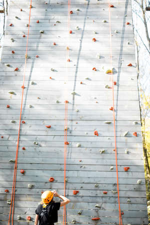 Young woman in sportswear and safety equipment looking on the climbing wall before climbing. Wide view from the backsideの写真素材