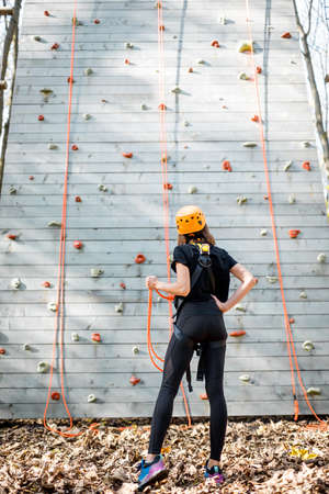 Young woman in sportswear and safety equipment looking on the climbing wall before climbing. View from the backsideの写真素材