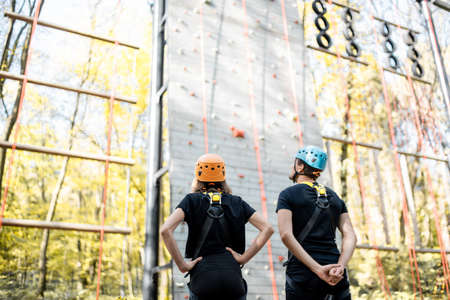 Well-equipped man and woman standing in front of the climbing wall outdoors, ready for the climbingの写真素材