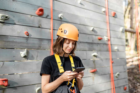 Young woman in protective sports equipment with a smart phone near the climbing wall outdoorsの写真素材