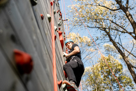 Well-equipped man climbing the wall outdoors in the park for sports entertainmentの写真素材