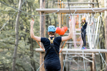 Well-equipped man and woman having an active recreation, climbing ropes in the park with obstacles...