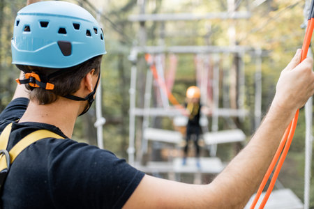 Well-equipped man having an active recreation, climbing in a rope park with obstacles in the forest,...