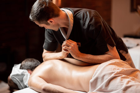 Professional masseur doing a deep back massage to a male client at Spa salon