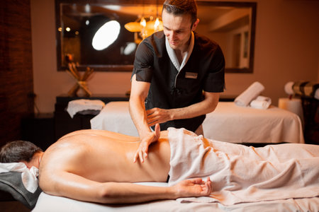 Professional masseur doing a deep back massage to a male client at Spa salonの写真素材