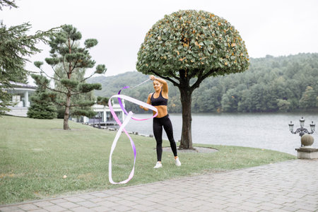 Athletic woman practising rhythmic gymnastics with a ribbon outdoors