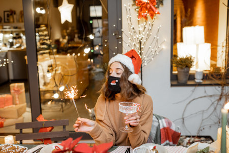 Young woman in facial mask celebrating alone New Year holidays at home. Concept of quarantine and self-isolation during the epidemic on holidaysの写真素材