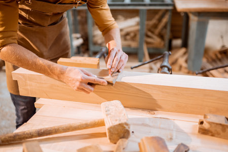 Carpenter working with a wood, marking plank with a pencil in a carpentry workshop, close-up viewの写真素材