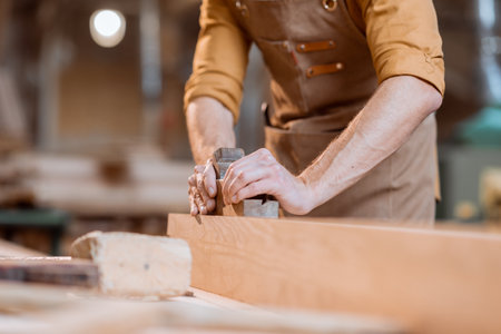 Carpenter working with a wood, planing a bar with a plane in the carpentry workshop. Close-up on handsの写真素材