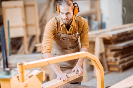 Carpentry worker sawing wooden planks with circular saw in the joinery warehouseの写真素材