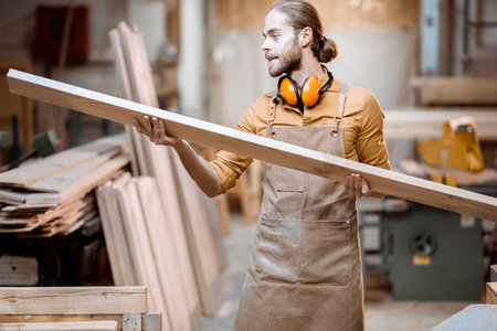 Handsome carpenter choosing planks for his woodwork at the joiners warehouseの写真素材