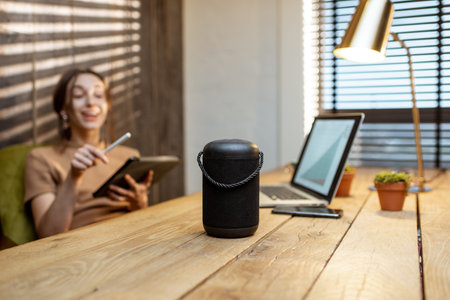 Woman talking to the smart speaker while working on the digital tablet at cozy home office. Concept...