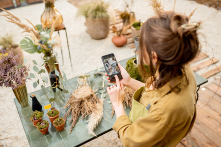 Woman photographing on a smartphone compositions of flowers and herbs during a floral workshop...