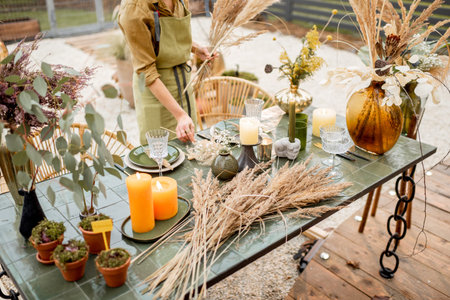 Young female putting herbs on the table, decorating tablescape in natural Boho style in green tones...